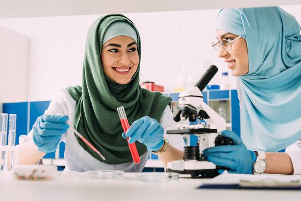 female muslim scientists with glass tube, pipette and microscope during experiment in chemical laboratory - Photo, Image