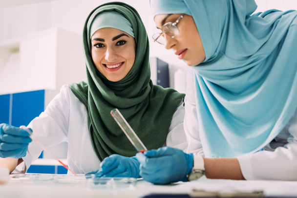 female muslim scientists holding pipette and glass test tube during experiment in chemical lab - Photo, Image