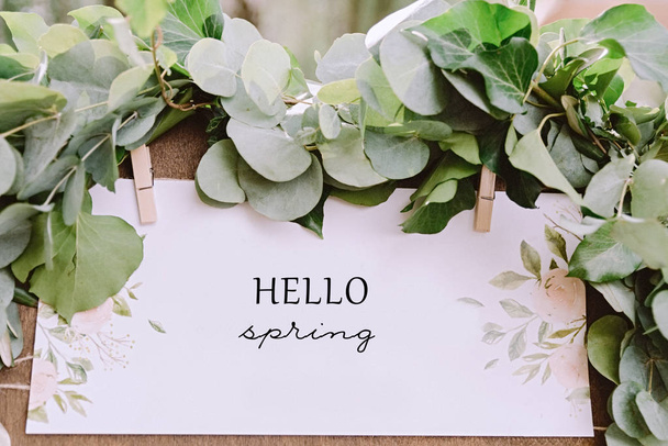. Ein weißer Karton auf einer Staffelei mit Eukalyptusgrün drumherum und dem Schild "Hallo Frühling" - Foto, Bild