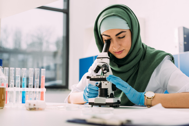 prachtige vrouwelijke islamitische wetenschapper op zoek via Microscoop tijdens experiment in chemisch laboratorium - Foto, afbeelding
