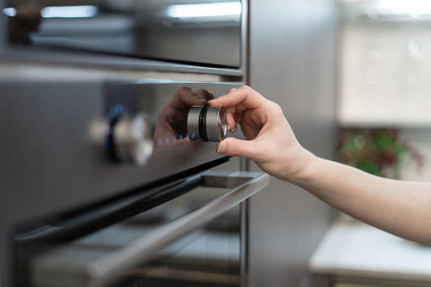 Vrouw hand programma inschakelen in het Configuratiescherm voor ingebouwde oven in moderne zwarte keukenkast - Foto, afbeelding