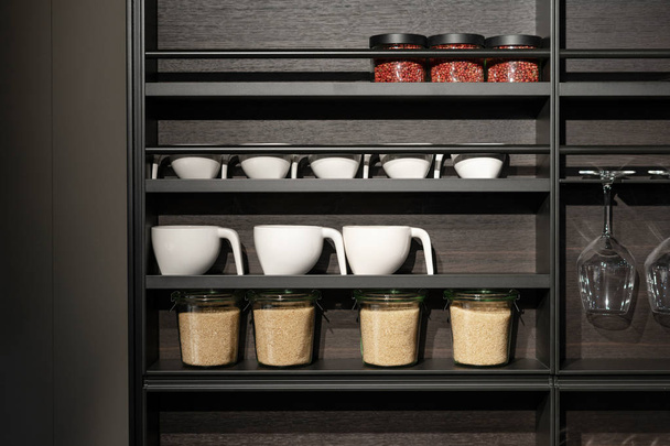 weißer Tee, Kaffeekeramik-Tasse und andere Gegenstände stehen auf schwarzem Küchenholzregal mit Designkomponente - Foto, Bild