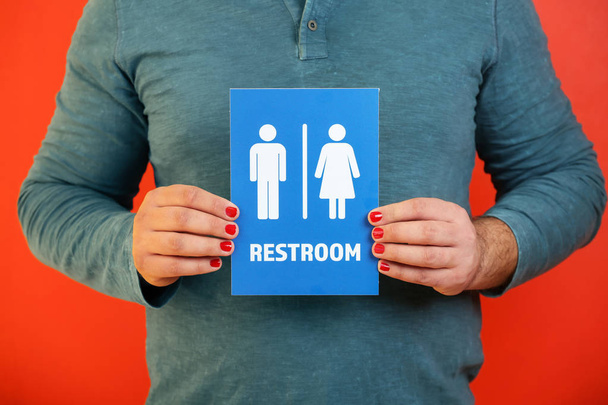 Man with manicure showing unisex restroom sign board on color background, closeup - Photo, Image