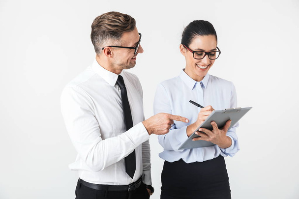 Couple of colleagues wearing formal clothing standing isolated over white background, working together, holding binder - Photo, image