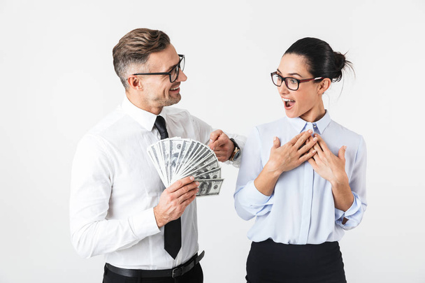 Couple of colleagues wearing formal clothing standing isolated over white background, holding money banknotes - Foto, Imagen