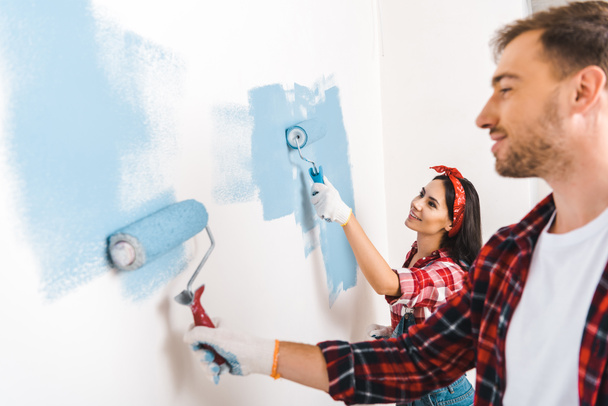 happy couple painting wall in blue color at home - Fotografie, Obrázek