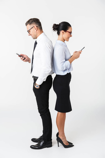 Full length of a colleagues couple wearing formal clothing standing isolated over white background, using mobile phone - Photo, Image