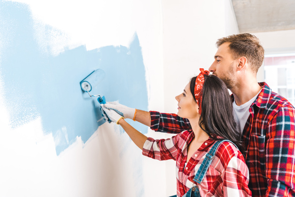 cheerful man and woman painting wall in blue color at home - Foto, Imagem