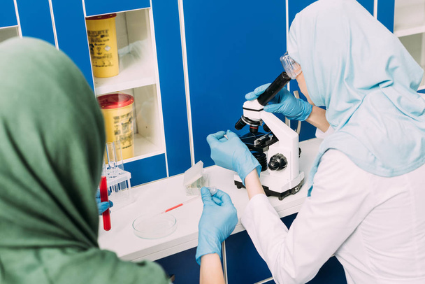 female muslim scientists with microscope, petri dish and pipette during experiment in chemical laboratory - Photo, Image