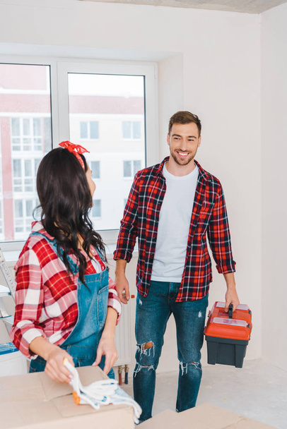 selective focus of cheerful man looking at woman while holding toolbox - Foto, Imagen