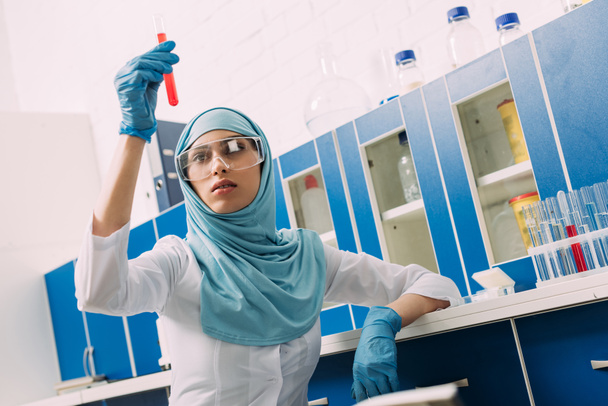 cientista muçulmano fêmea em óculos segurando tubo de ensaio com líquido vermelho em laboratório
 - Foto, Imagem