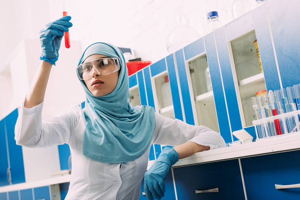 mujer musulmana científica en gafas que sostiene el tubo de ensayo con líquido rojo en laboratorio
 - Foto, Imagen
