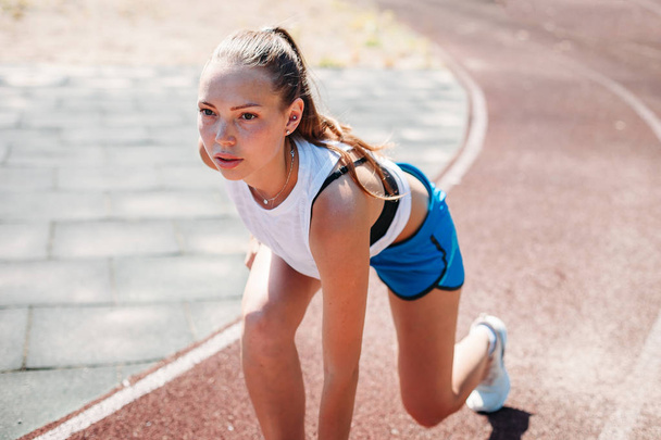 Young athletic woman preparing to run at the stadium, outdoors. The concept of a healthy lifestyle - 写真・画像