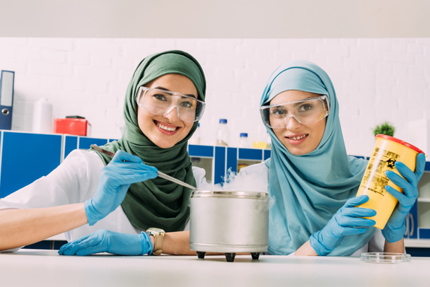 θηλυκό μουσουλμάνων επιστημόνων στα γυαλιά βλέπουν φωτογραφική μηχανή πειραματιμένος με ξηρό πάγο σε χημικό εργαστήριο - Φωτογραφία, εικόνα