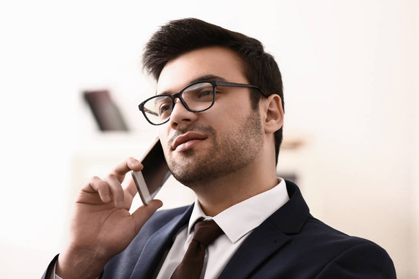 Handsome young businessman talking by mobile phone in office - 写真・画像