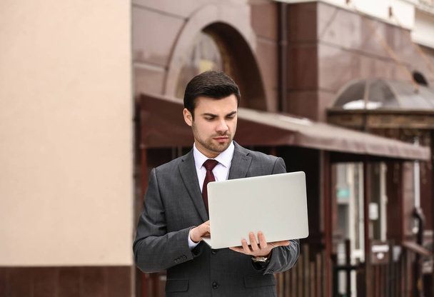 Portrait of handsome young businessman with laptop outdoors - Foto, afbeelding
