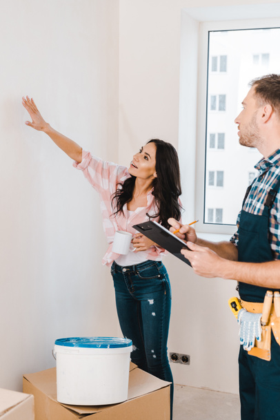 selective focus of attractive woman showing wall to handyman  - Foto, afbeelding