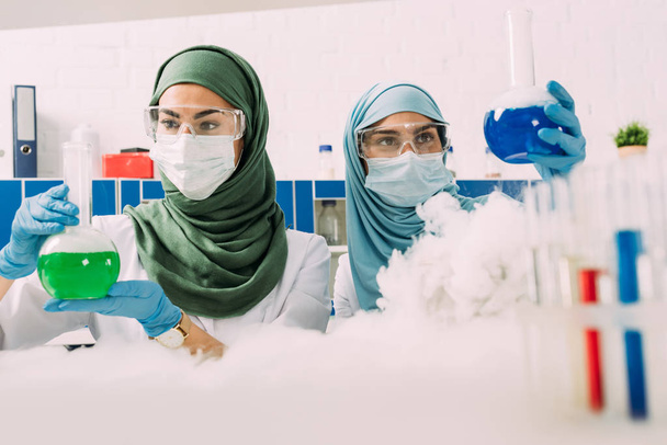 female muslim scientists holding flasks while experimenting with dry ice in chemical laboratory - Photo, Image