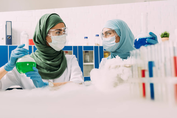 Muslimische Wissenschaftlerinnen halten Fläschchen, während sie im Chemielabor mit Trockeneis experimentieren - Foto, Bild