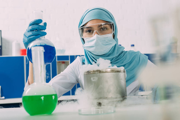Muslimische Wissenschaftlerin hält Fläschchen während Experiment mit Trockeneis im Chemielabor - Foto, Bild