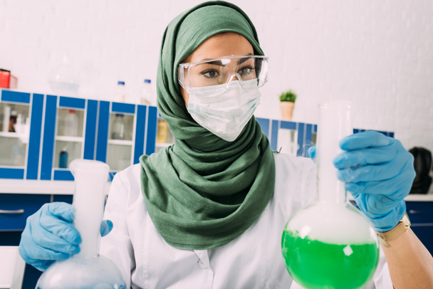 mujer musulmana científica sosteniendo frascos durante el experimento en laboratorio químico
 - Foto, Imagen