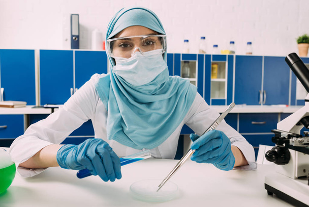 mujer musulmana científica mirando la cámara, sosteniendo el tubo de ensayo y experimentando con hielo seco en el laboratorio
 - Foto, Imagen