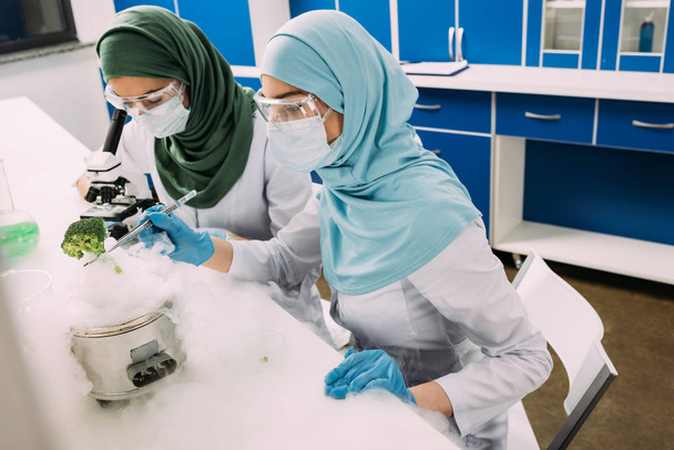 θηλυκό μουσουλμάνων επιστημόνων πειραματίζεται με τον ξηρό πάγο και χρησιμοποιώντας μικροσκόπιο σε χημικό εργαστήριο - Φωτογραφία, εικόνα
