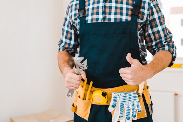 cropped view of handyman holding wrench and showing thumb up - 写真・画像
