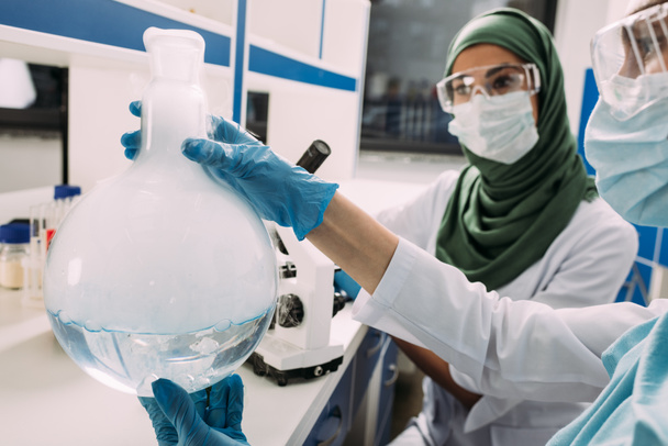 científicas musulmanas en gafas que sostienen el frasco con líquido mientras experimentan en laboratorio químico
 - Foto, Imagen