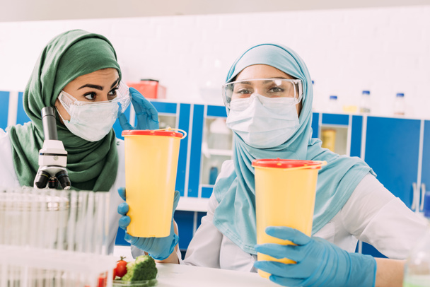 femmes musulmanes scientifiques tenant des conteneurs de déchets cliniques et regardant la caméra en laboratoire chimique
 - Photo, image