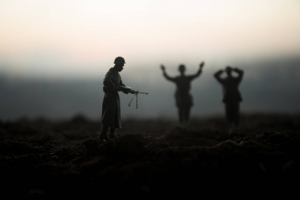 Cena de batalha. Silhuetas militares lutando cena no fundo do céu de nevoeiro de guerra. Um soldado alemão levantou armas para se render. Soldados de brinquedo de plástico com armas que levam prisioneiro o soldado inimigo. Obra de arte
 - Foto, Imagem