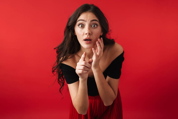 Photo of a beautiful shocked young woman standing isolated over red wall background pointing to you. - Fotó, kép