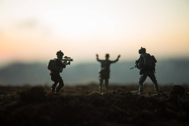 Battle scene. Military silhouettes fighting scene on war fog sky background. A German soldiers raised arms to surrender. Plastic toy soldiers with guns taking prisoner the enemy soldier. Artwork - Photo, Image