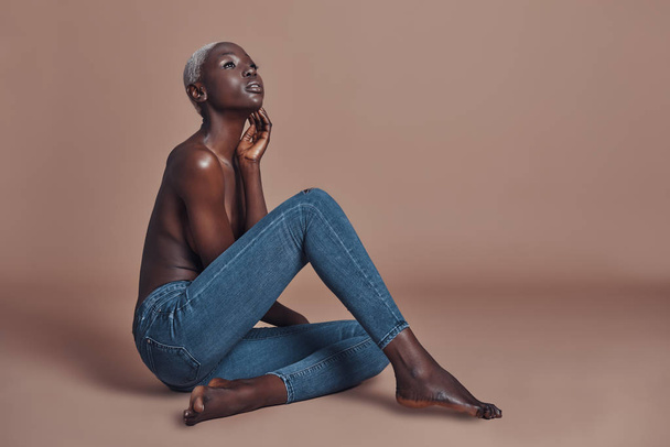 Attractive young African woman looking away while sitting against brown background - Fotó, kép