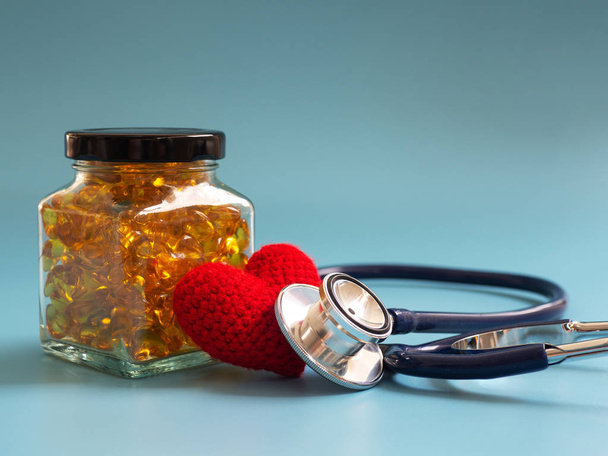 Red heart and stethoscope beside Fish oil capsules in glass bottles on blue background. Healthy omega-3 and stethoscope. - Фото, зображення