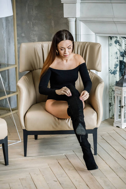 Portrait of beautiful young woman in black clothes. Young model sitting on armchair at luxury apartments interior - Valokuva, kuva