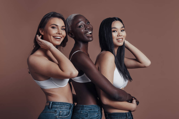 happy smiling three women wearing bras and posing against brown background and looking at camera - Photo, image