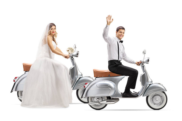 Full length shot of a bride and groom riding vintage scooters and waving isolated on white background - Foto, Bild