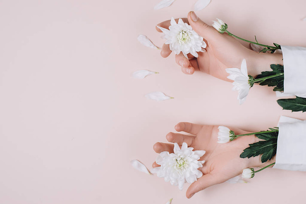 Creative and fashion art skin care of hands and white flowers in hands of women. Female hand with white flowers on pink background. Cosmetics for hands anti wrinkle. Flat lay, top view, copy space - Фото, изображение