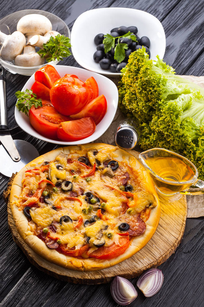 Herkullinen Kotitekoinen pizza ja ainesosat tarjoillaan musta puinen pöytä
 - Valokuva, kuva