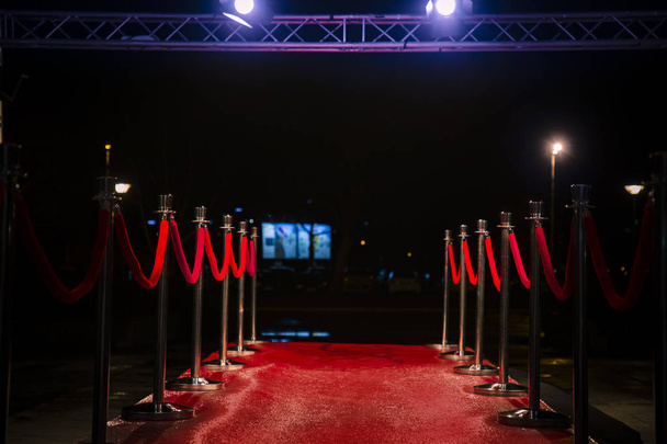 Roter Teppich mit Barrieren, Samtseilen und Lichtern im Hintergrund - Foto, Bild
