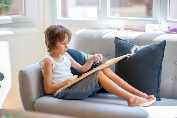 Niño preescolar, leyendo un libro y jugando con un juguete educativo de madera
 - Foto, imagen