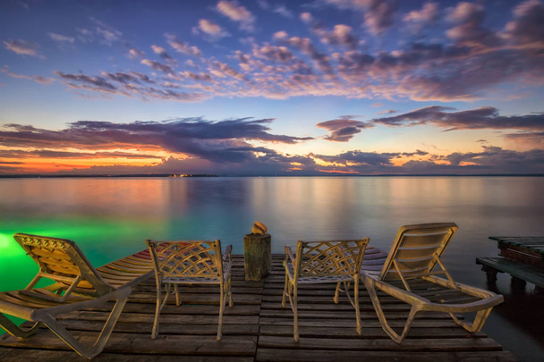 Sillas y tumbonas vacías en un muelle de madera esperando el amanecer en la playa del mar
. - Foto, Imagen
