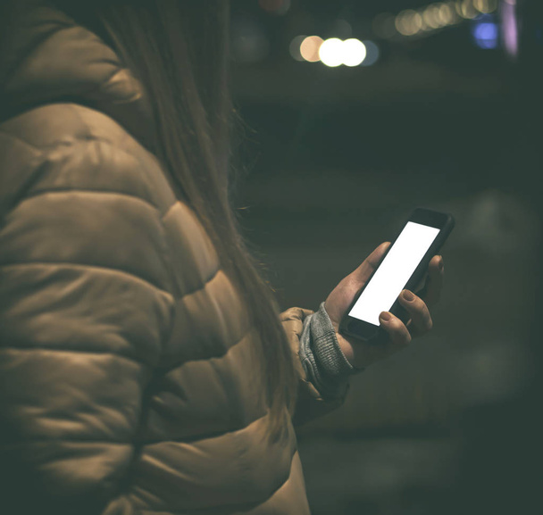 La giovane donna tiene il telefono e legge qualche testo nella città serale in inverno.
 - Foto, immagini