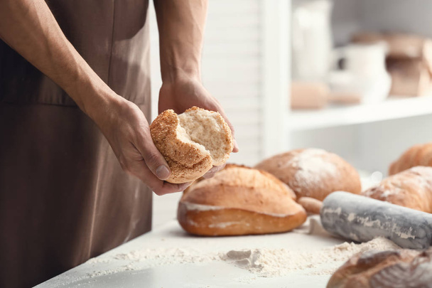 Young man breaking freshly baked bun in kitchen - Foto, afbeelding