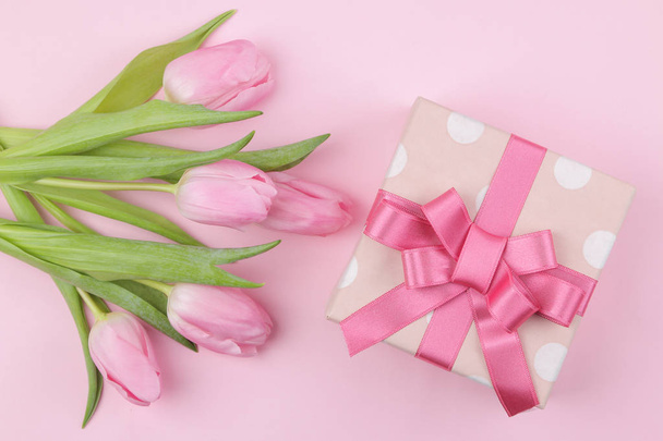 Un ramo de hermosas flores de tulipanes rosados y una caja de regalo sobre un fondo rosa de moda. Primavera. vacaciones. vista superior
. - Foto, Imagen