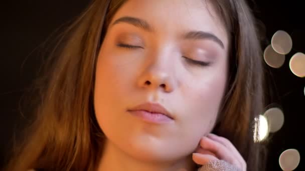 Close-up retrato de jovem caucasiana menina com olhos fechados e movendo a cabeça em satisfação no fundo luzes borradas
. - Filmagem, Vídeo