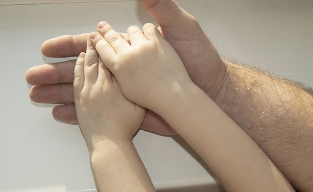Le père tenant soigneusement dans sa main la main d'un enfant. Bonne famille, soins et amour, fête des pères. - Photo, image