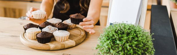weergave van de serveerster zetten cupcakes op houten dienblad in koffiehuis bijgesneden - Foto, afbeelding
