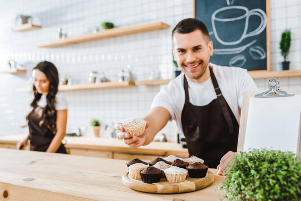 valikoiva painopiste komea barista antaa cupcake wile kassanhoitaja työskentelee kahvilassa
 - Valokuva, kuva